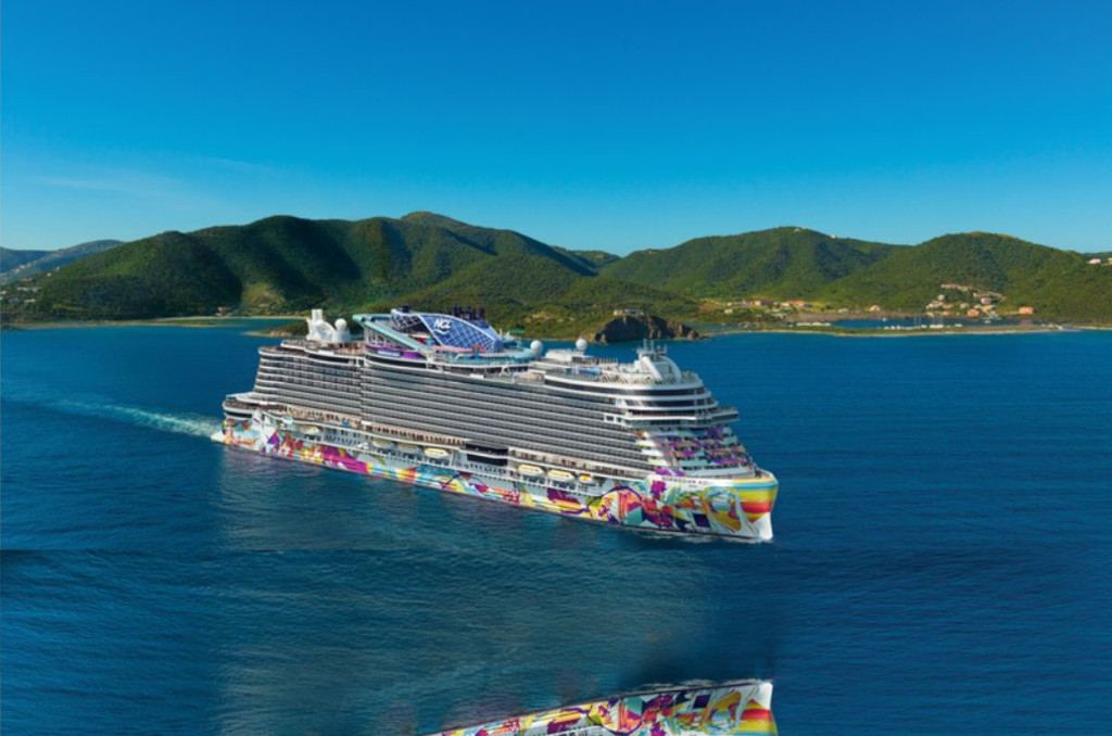 Das Kreuzfahrtschiff Norwegian Aqua mit bunt bemaltem Rumpf fährt auf blauem Meer vor einer grünen Inselkulisse. Das Kreuzfahrtschiff Norwegian Aqua mit bunt bemaltem Rumpf fährt auf blauem Meer vor einer grünen Inselkulisse.